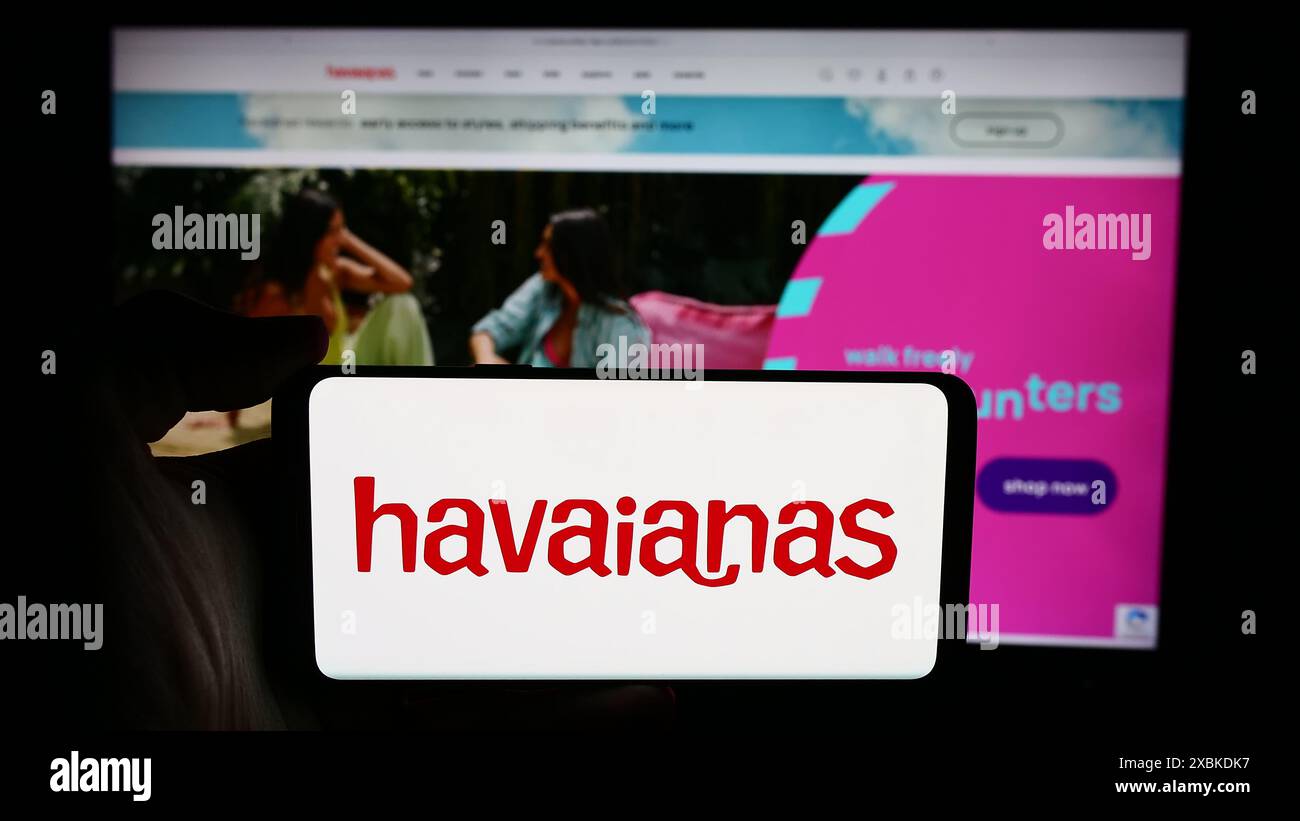 Person, die ein Handy mit dem Logo des brasilianischen Flipflop-Herstellers Havaianas vor der Business-Webseite hält. Schwerpunkt auf dem Display des Telefons. Stockfoto