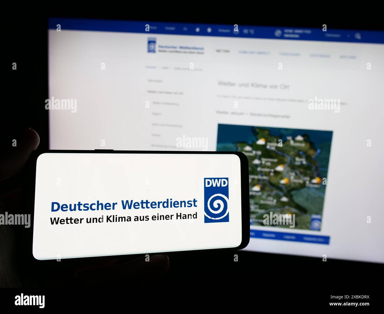 Person mit Smartphone und Logo des Deutschen Wetterdienstes (DWD) vor der Website. Schwerpunkt auf dem Display des Telefons. Stockfoto