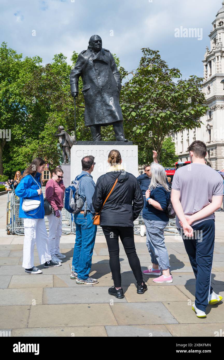 Touristen mit Reiseleiter stehen mit Blick auf die Statue von Sir Winston Churchill am Parliament Square Garden Westminster London England Großbritannien Stockfoto