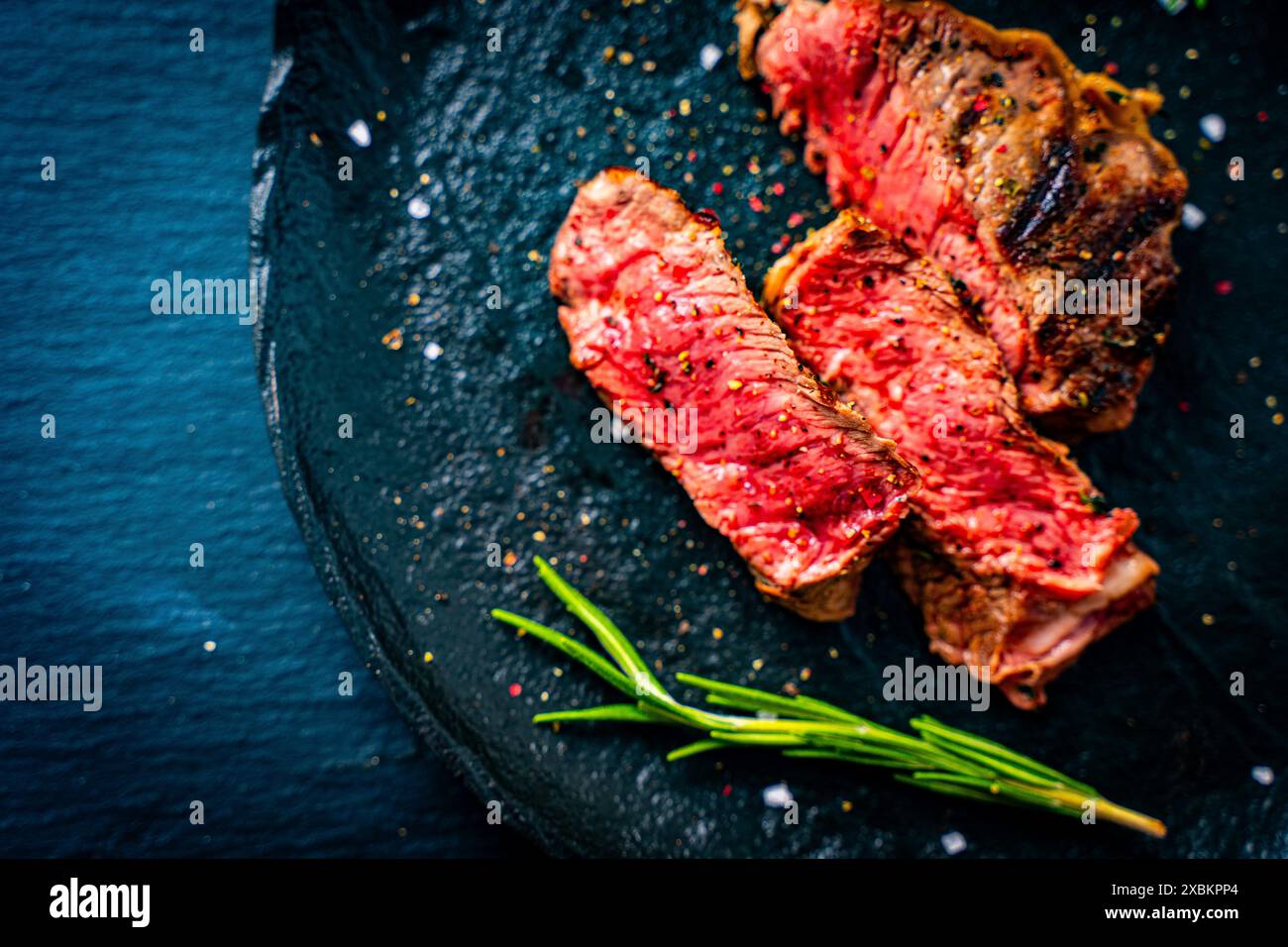 Mittelseltenes marmoriertes Rindersteak, geschnitten mit Rosmarin und Gewürzen auf einer schwarzen Platte. Hochwertige Fotos Stockfoto