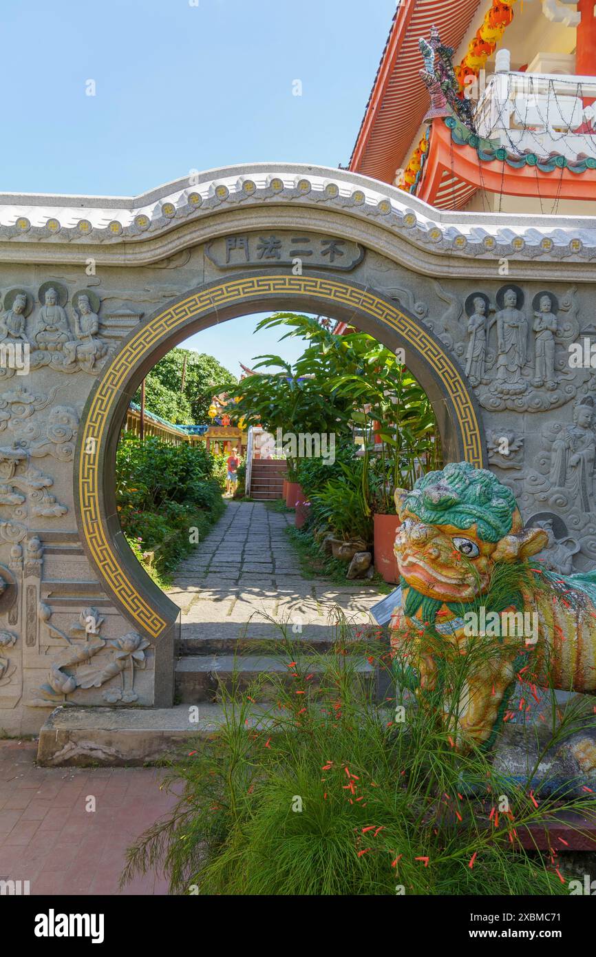 Ein dekorativer Steinbogen mit einer Skulptur eines Löwen in einem traditionellen Tempelgarten mit umgebender Vegetation, Pattaya, Thailand Stockfoto