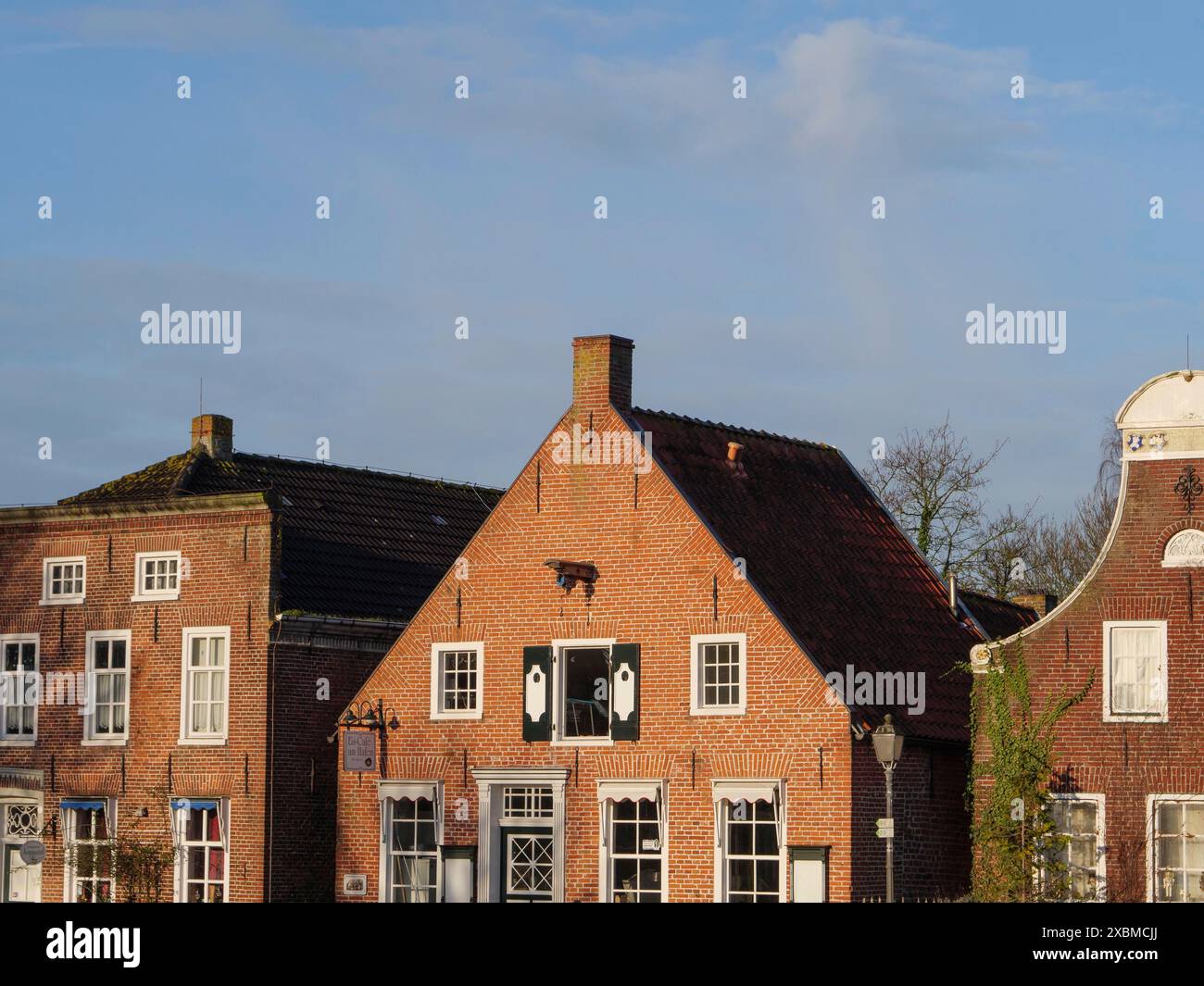 Drei historische Backsteinhäuser mit verschiedenen Dachformen unter klarem blauen Himmel, greetsiel, ostfriesland, deutschland Stockfoto