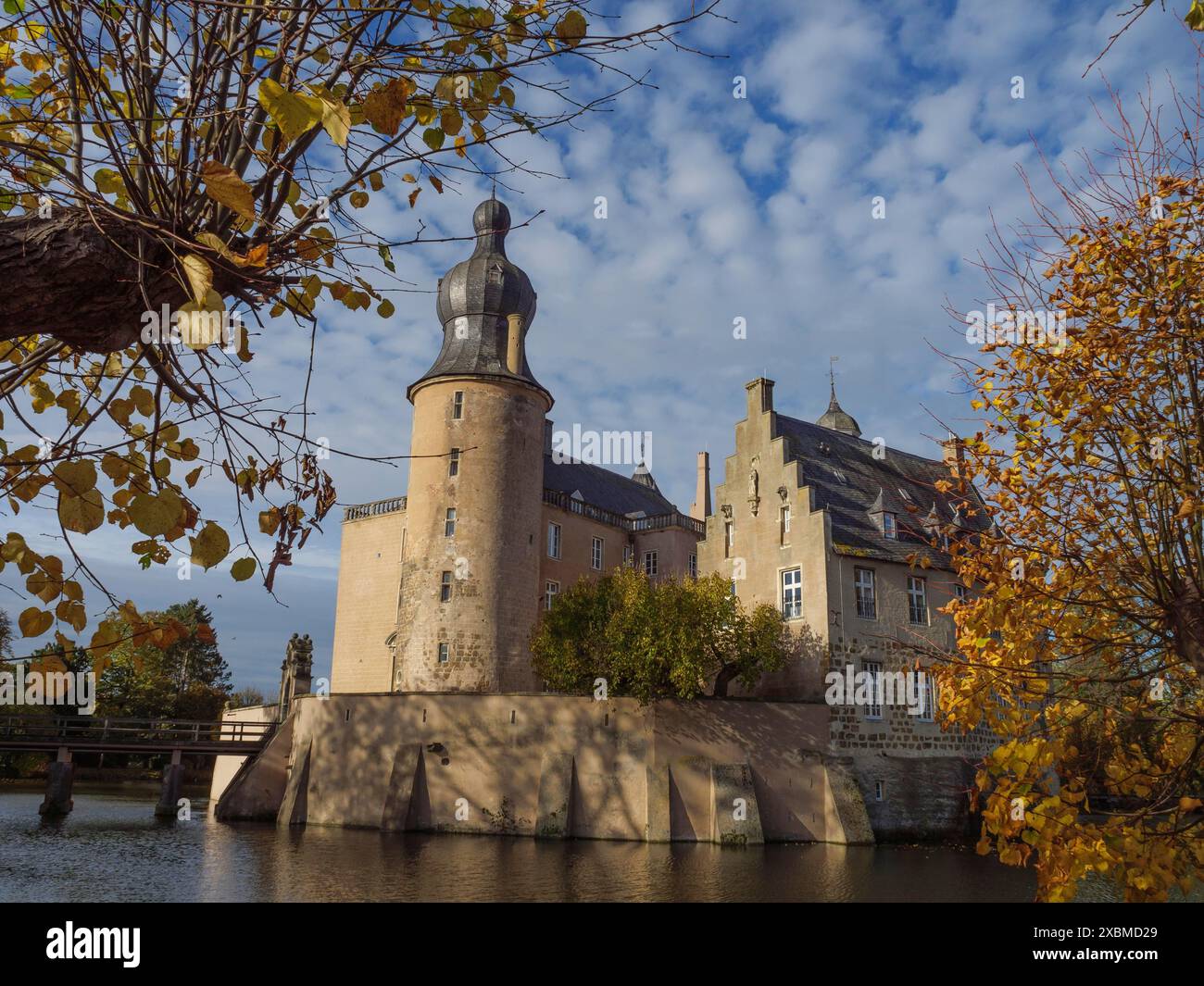 Eine malerische Burg im Herbst, umgeben von Wasser und Bäumen mit Orangenblättern, unter teilweise bewölktem Himmel, Gmen, münsterland, westfalen, deutschland Stockfoto