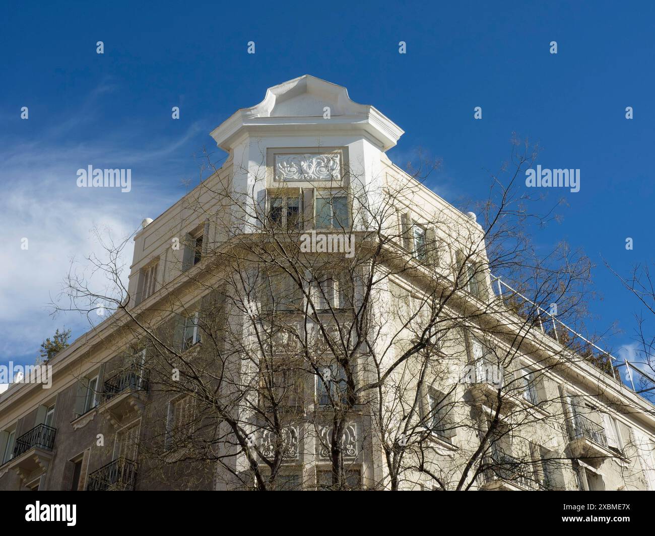 Ein mehrstöckiges Gebäude mit dekorativen Elementen. Der Himmel ist klar und blau, und ein unbelaubter Baum fällt hervor, Madrid, Spanien Stockfoto