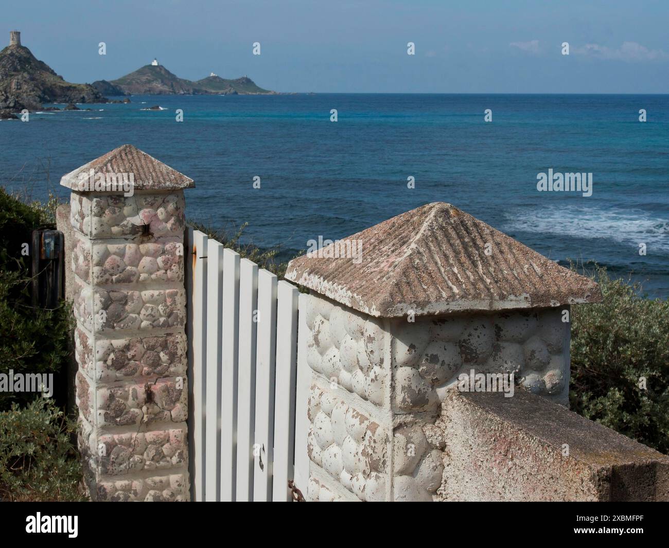 Weißes Tor mit Steinsäulen mit Blick auf das Meer mit Hügeln im Hintergrund, ajaccio, korsika, frankreich Stockfoto