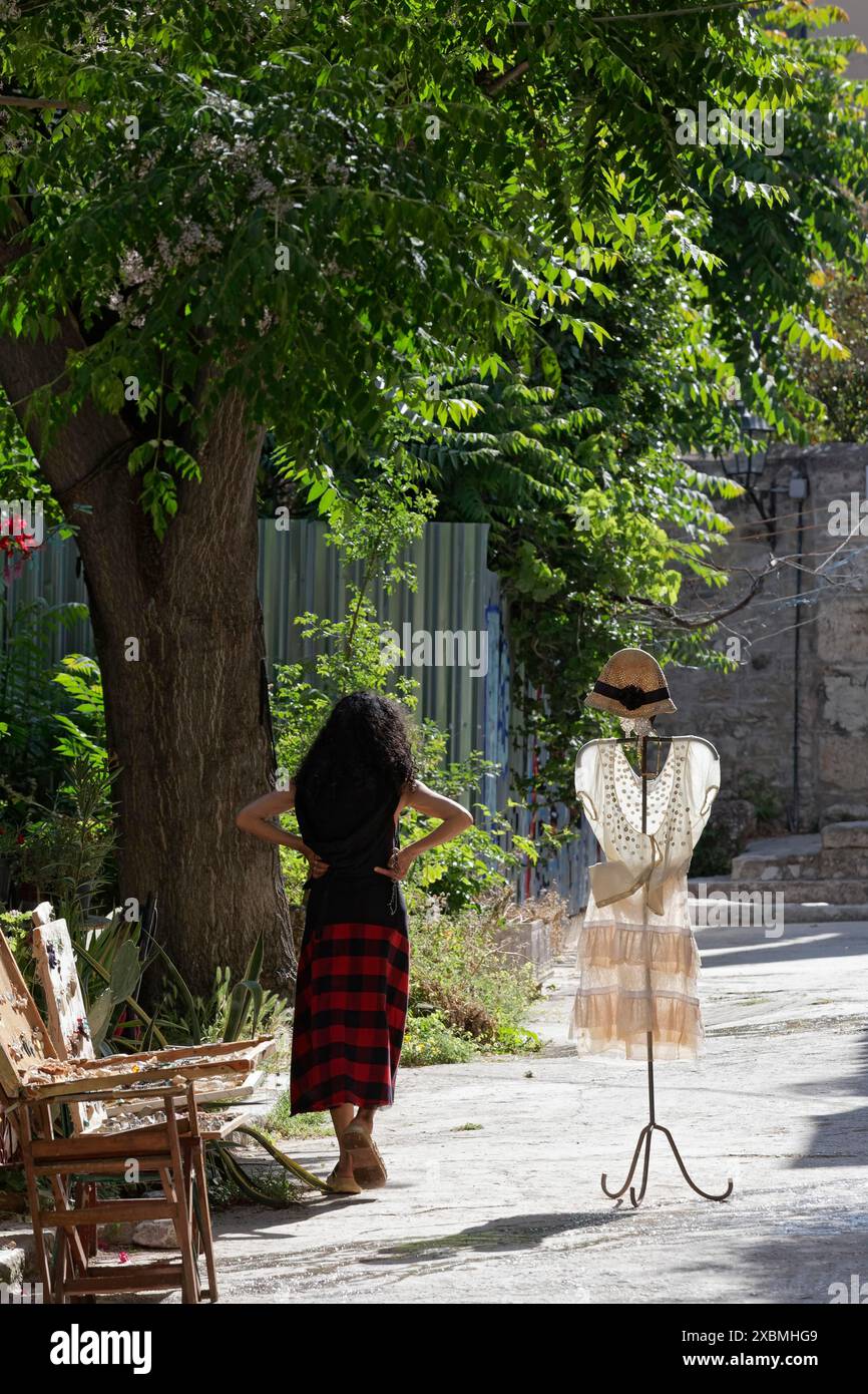 Kleiderständer mit Sommerkleid im Morgenlicht, vor einer Modeboutique platziert, Frau wartet auf Kunden, Plaka Viertel, Athen Stockfoto