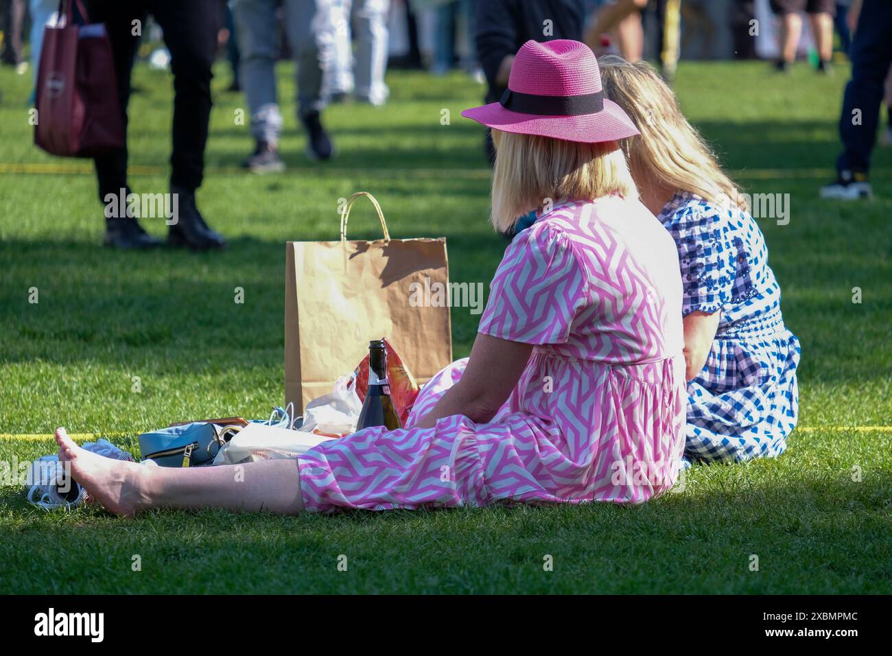 Zwei Frauen in Sommerkleidern genießen einen warmen Nachmittag in den Parliament Square Gardens mit einer Flasche Wein. Stockfoto