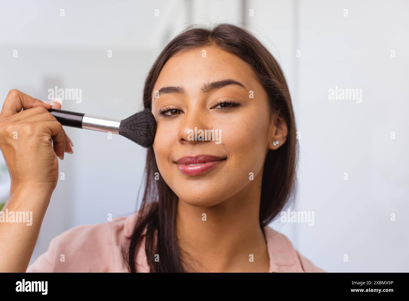 Biracial glückliche Frau, die Make-up mit Pinsel aufträgt, selbstbewusst lächelt Stockfoto