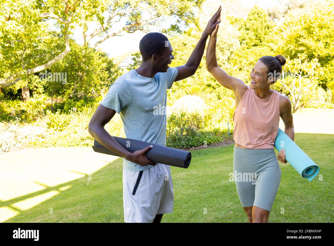 Glückliches vielseitiges Paar High-Fiving mit Yogamatten, Wellness und gesundem Lebensstil Stockfoto