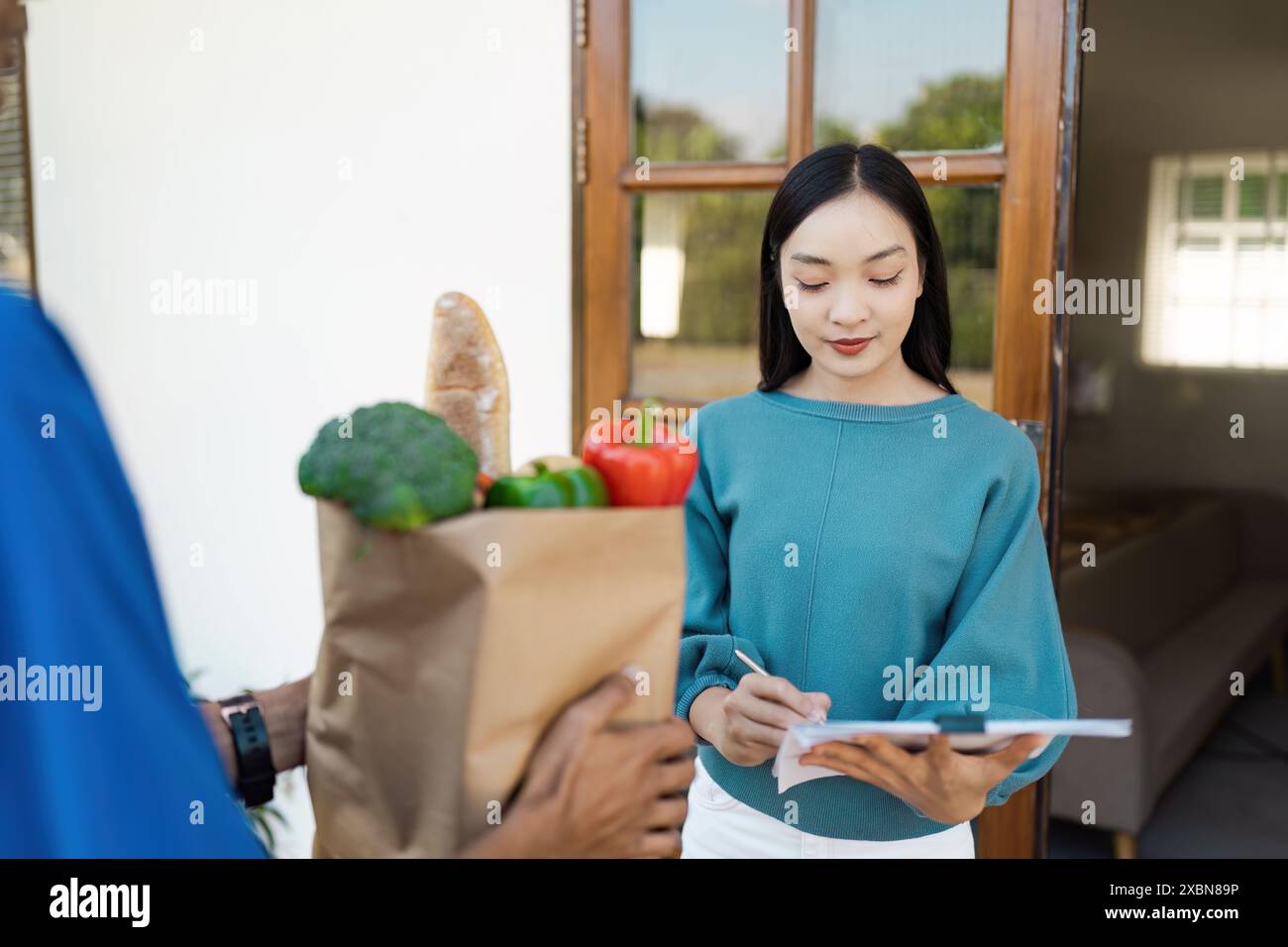 Lieferservice nach Hause: Kunde erhält ein Lebensmittelpaket und unterzeichnet die Lieferbestätigung Stockfoto