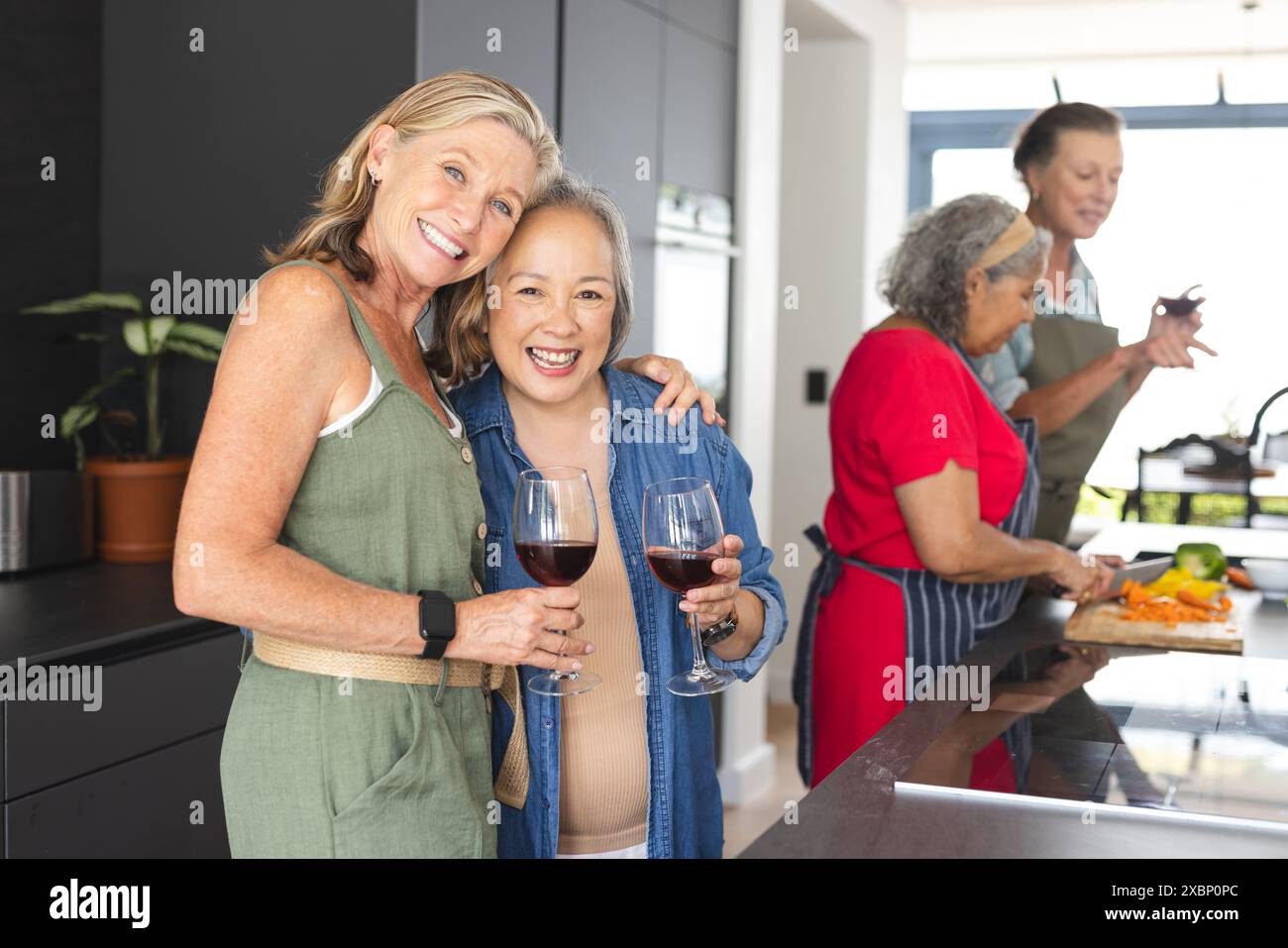 Verschiedene Gruppe reifer Frauen, die Wein genießen und gemeinsam Essen in der Küche zubereiten Stockfoto