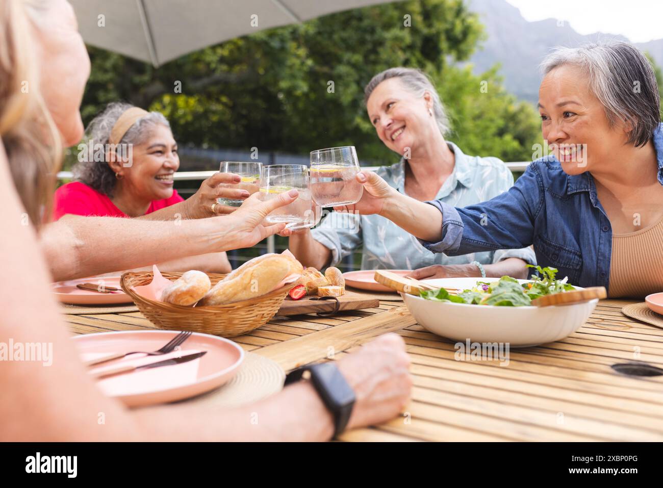 Eine Gruppe verschiedener Seniorinnen genießt gemeinsam Getränke und Essen am Tisch im Freien Stockfoto