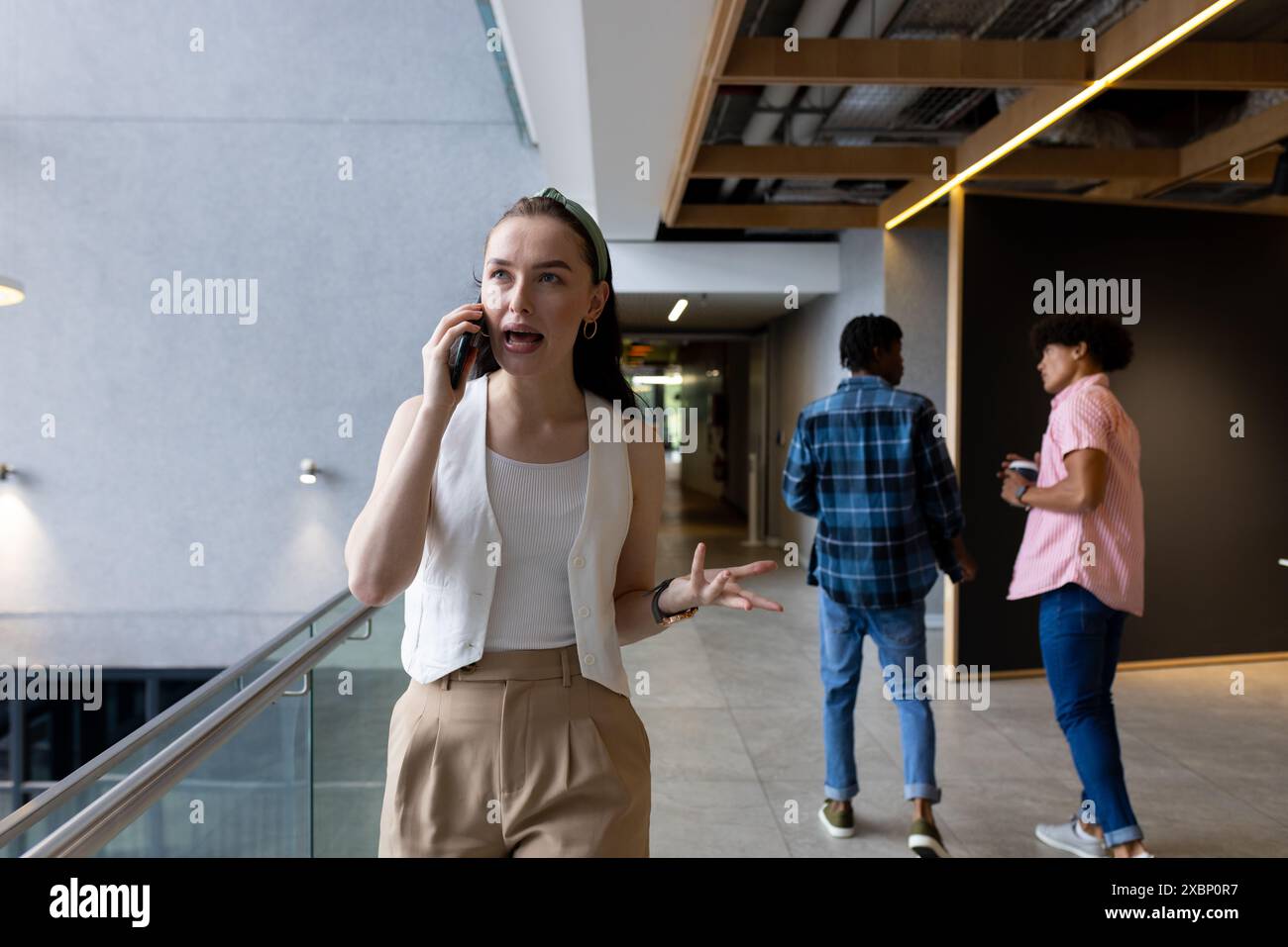 Kaukasische Frau, die auf dem Smartphone spricht, im Flur des Büros läuft, geschäftlich Stockfoto