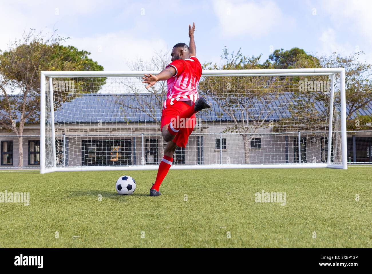 Afroamerikanischer Fußballspieler, der Fußball auf dem Feld kickt und stark und fit wirkt Stockfoto