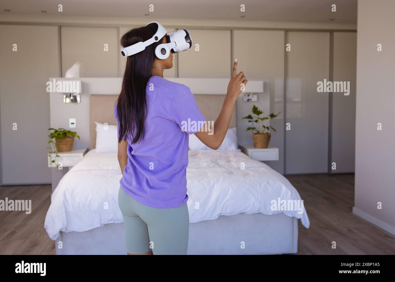 Glückliche birassische Frau mit Virtual-Reality-Headset im modernen Schlafzimmer Stockfoto