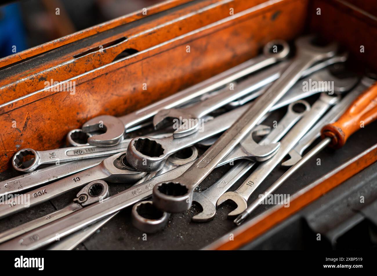 Hoher Winkel von verschiedenen mechanischen Hardware-Werkzeugen und Instrumenten sowie Schraubendreher in schäbiger Ölkiste in der Werkstatt vor verschwommenem Hintergrund Stockfoto