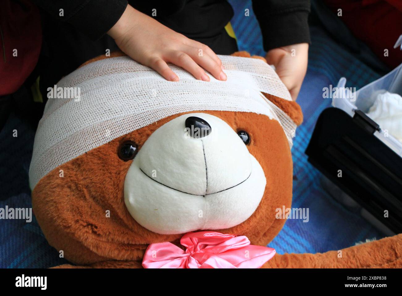 Einen Teddybären pflegen - Kinderhände legen einen Verband auf den Kopf des Bären Stockfoto