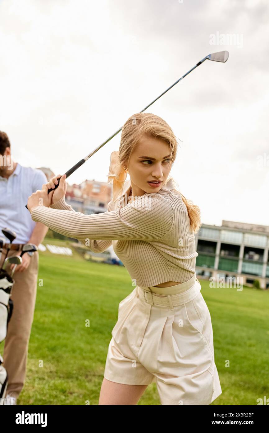 Eine Frau in elegantem Gewand schwingt einen Golfclub vor einem Mann auf einem grünen Feld und verkörpert einen Zeitvertreib der Oberschicht. Stockfoto