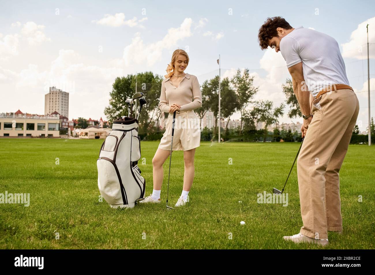 Ein Mann und eine Frau, elegant gekleidet, genießen eine Runde Golf auf einem üppigen grünen Feld und verkörpern einen gehobenen Lebensstil. Stockfoto