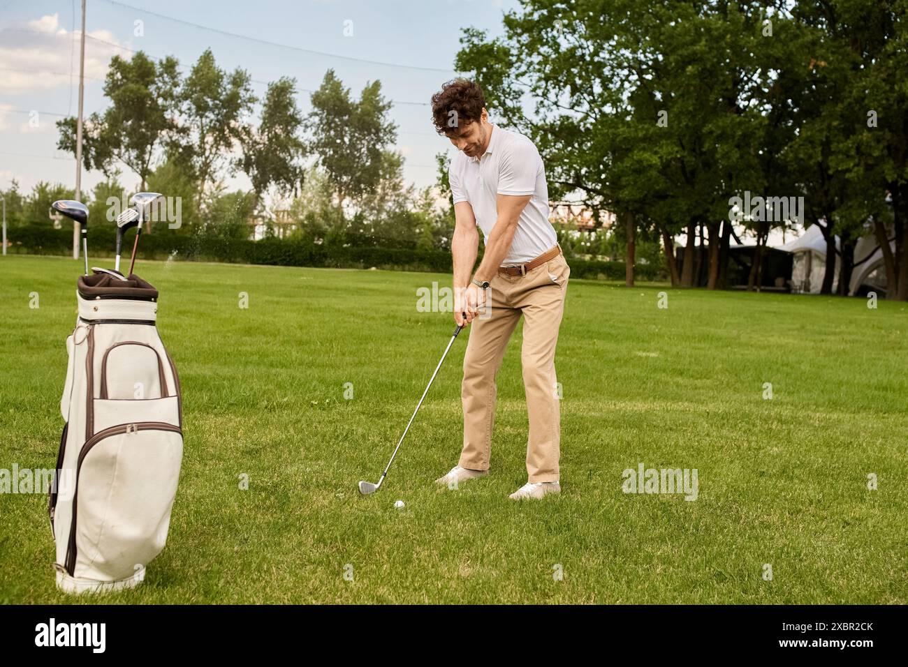 Ein Mann in eleganter Kleidung schwingt einen Golfclub auf einem grünen Feld, Freizeit der gehobenen Klasse. Stockfoto