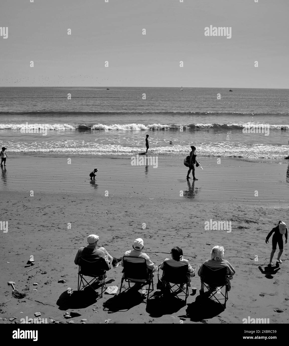 Vier Rentner saßen hintereinander am Strand vor der Cobble Landing in Filey, North Yorkshire East Coast, Nordengland, Großbritannien Stockfoto