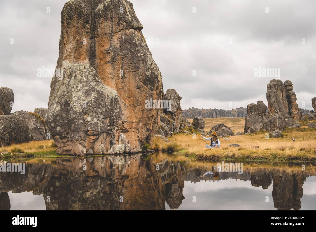 Eine Frau sitzt auf einem Feld neben einem Fluss, touristisch in den peruanischen anden, Huaillay, Pasco, Peru. Stockfoto