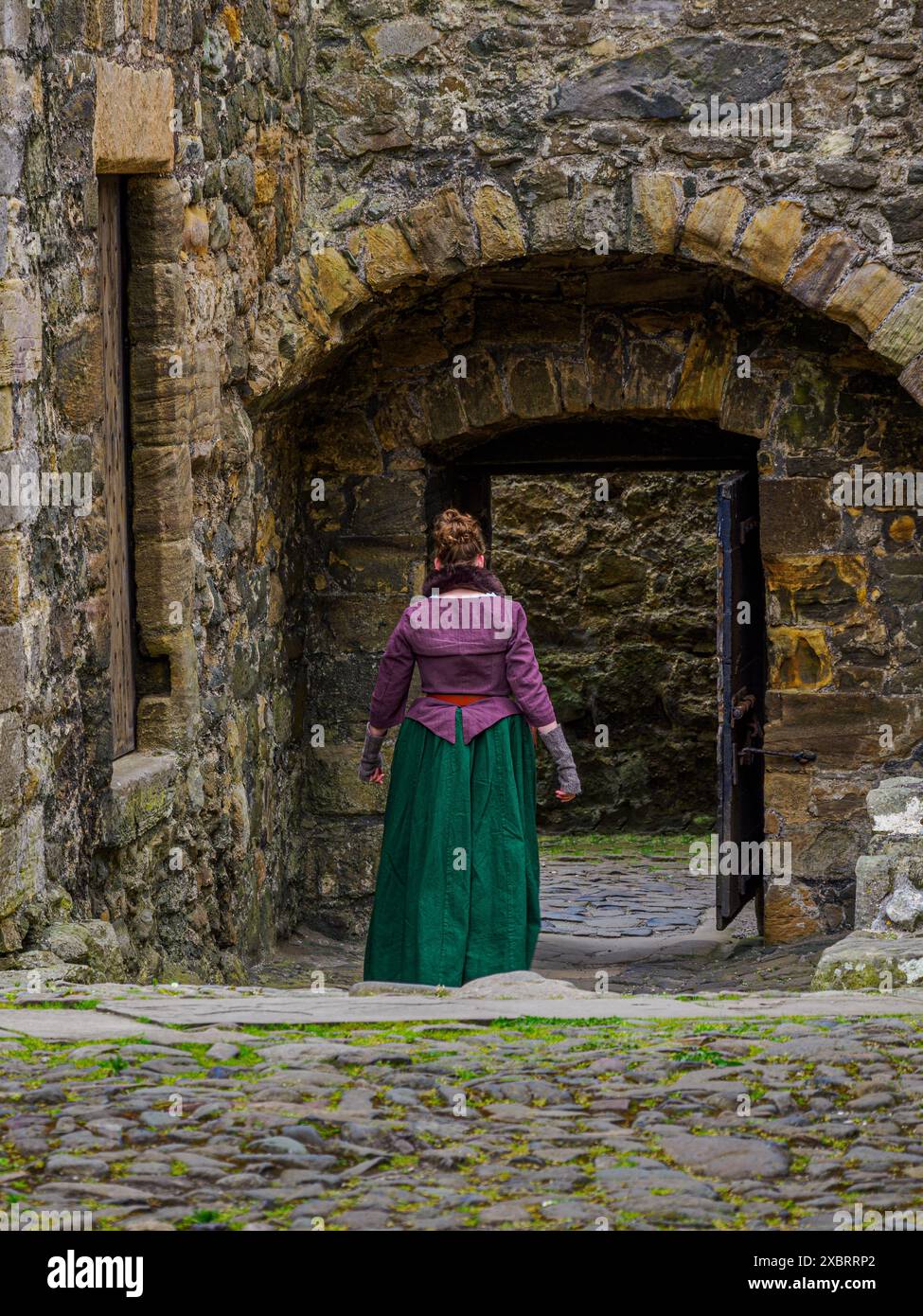 Ein Model in zeitgenössischer Kleidung geht über den Innenhof zum Haupttor von Blackness Castle Stockfoto