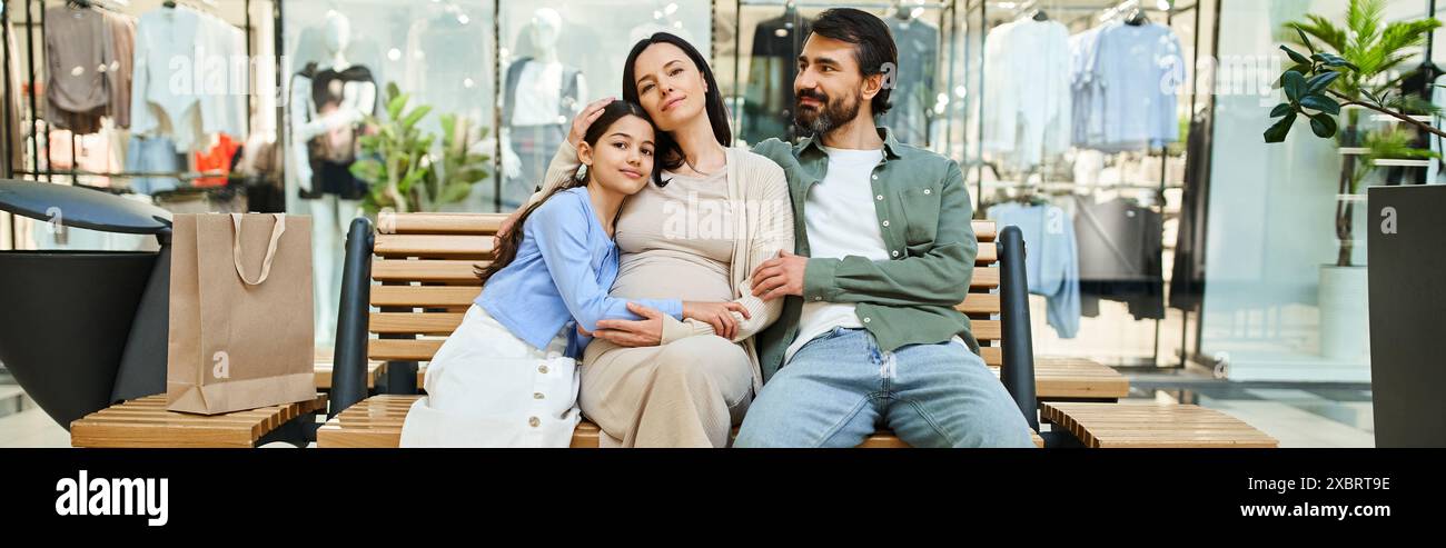 Ein Mann und eine Frau entspannen sich auf einer Bank mit Kind in einem geschäftigen Einkaufszentrum und machen eine Pause von ihrem Einkaufsausflug. Stockfoto