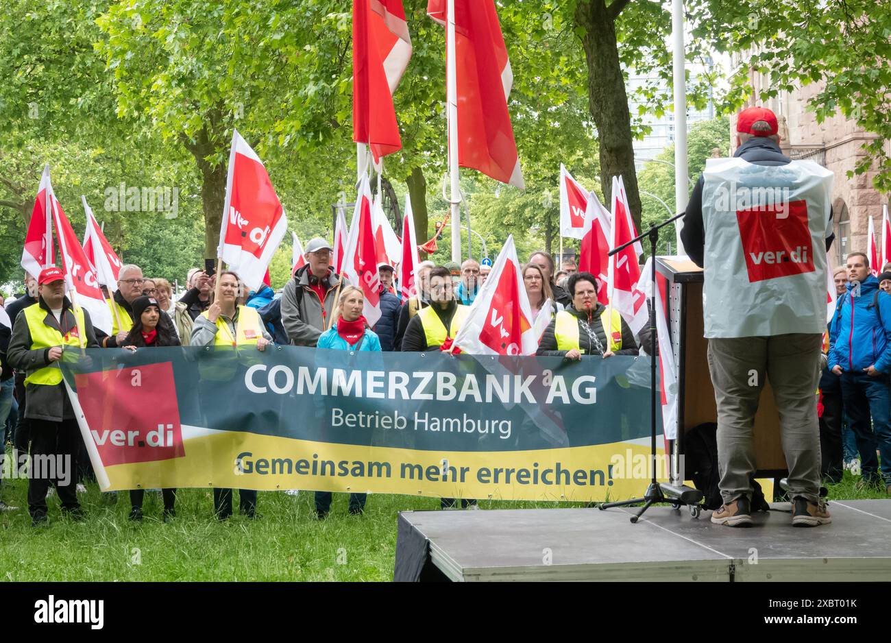 13. Juni 2024, Hamburg: Während eines Warnstreiks gegen mehrere Banken stehen Streikende mit Fahnen und Bannern bei einer Kundgebung zusammen. Auf einem Banner steht „gemeinsam mehr erreichen!“. Im Vorfeld der zweiten Tarifrunde hat Verdi die Mitarbeiter der Unicredit, der Deutschen Bank und der Commerzbank in Hamburg zu einem tagelangen Warnstreik aufgerufen. Foto: Bodo Marks/dpa Stockfoto