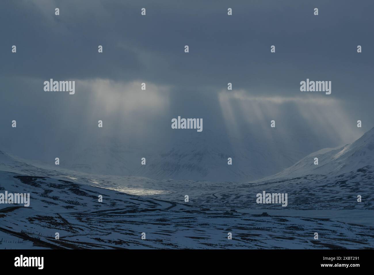 Sonnenlicht strömt durch Wolken über verschneite Berge Stockfoto