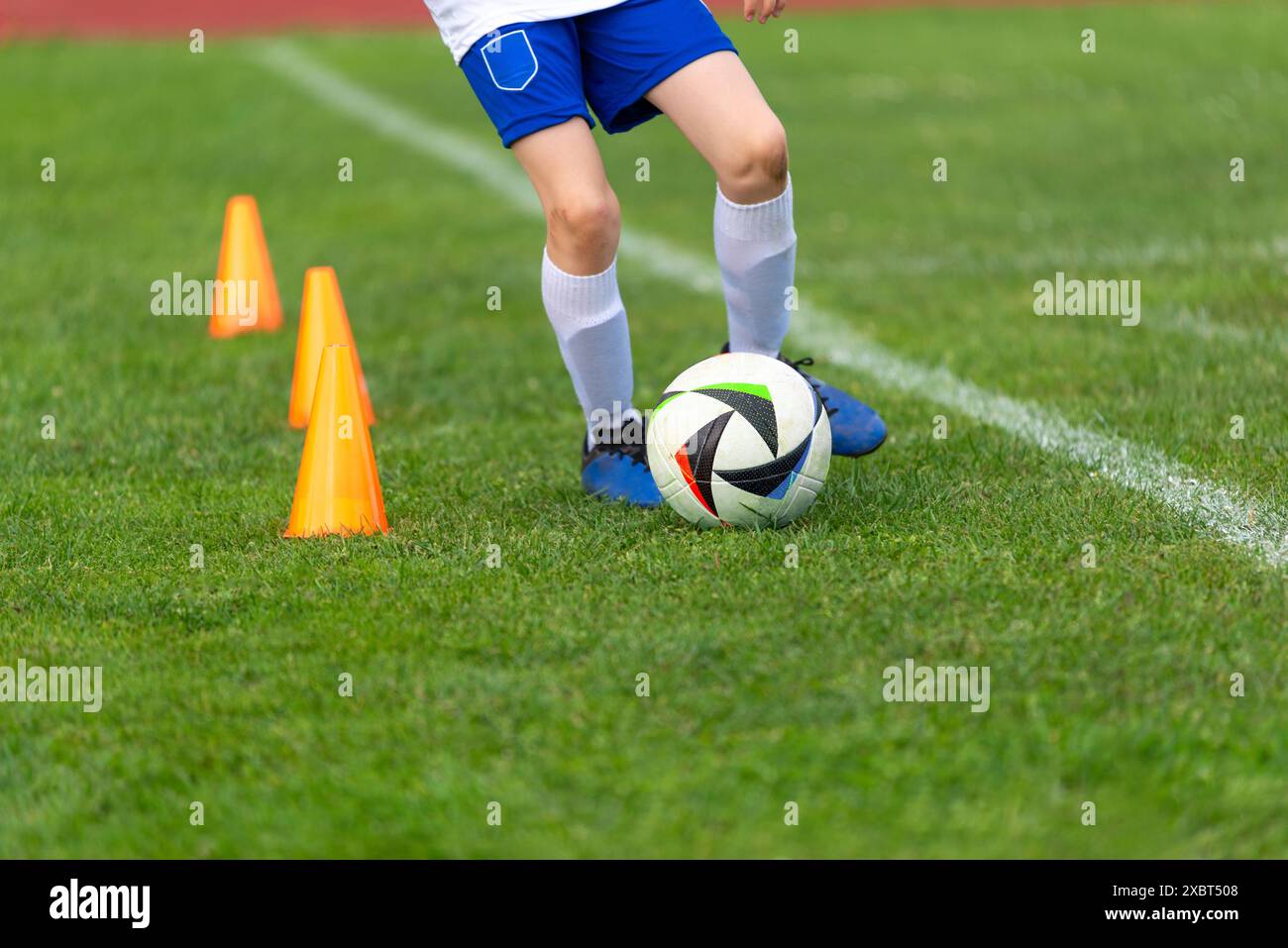 Fußballspieler im Training, der auf dem Feld in Nahaufnahme um Kegel geht. Ideal für Kinder im Sport, gesundes Leben, Aufwachsen, Erfolg und harte Arbeit Stockfoto