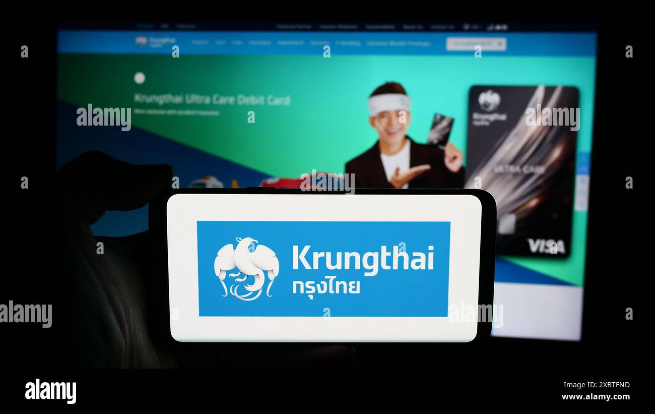 Person mit Handy mit Logo des thailändischen Unternehmens Krungthai Bank Public Company Limited vor der Webseite. Schwerpunkt auf dem Display des Telefons. Stockfoto