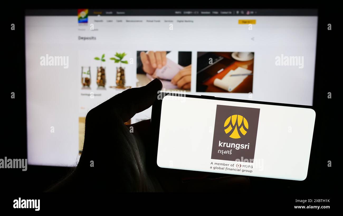 Person mit Smartphone und Logo der Thai Bank of Ayudhya Public Company Limited (Krungsri) vor der Website. Schwerpunkt auf dem Display des Telefons. Stockfoto