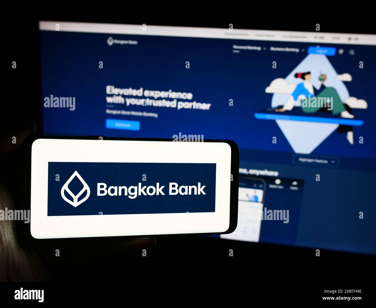 Person, die ein Mobiltelefon mit dem Logo der Thai Bangkok Bank Public Company Limited vor der Business-Webseite hält. Schwerpunkt auf dem Display des Telefons. Stockfoto