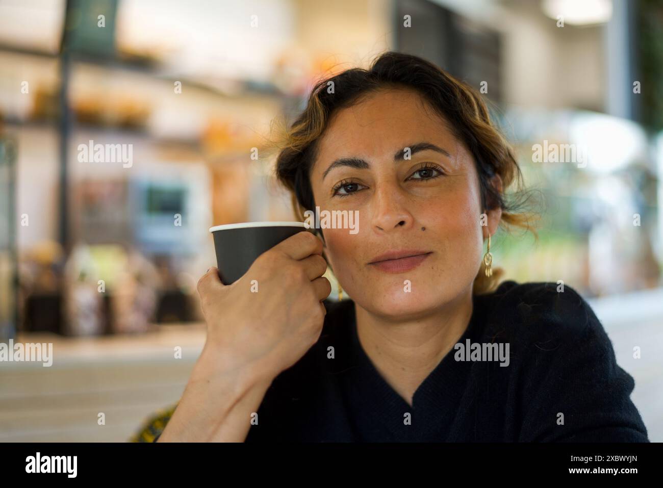 Eine selbstbewusste kolumbianische Frau, die in einem Café sitzt und Kaffee trinkt und direkt in die Kamera blickt. Augenkontakt. Kopierbereich Stockfoto