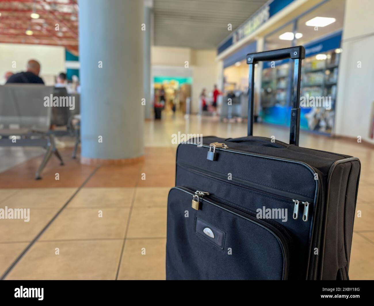Im Vordergrund steht ein weicher schwarzer Reisekoffer, im Hintergrund ein verschwommener Duty-Free-Shop am Flughafen, der den Beginn der Reise unterstreicht. Stockfoto Im Vordergrund steht ein weicher schwarzer Reisekoffer, im Hintergrund ein verschwommener Duty-Free-Shop am Flughafen, der den Beginn der Reise unterstreicht. Stockfoto