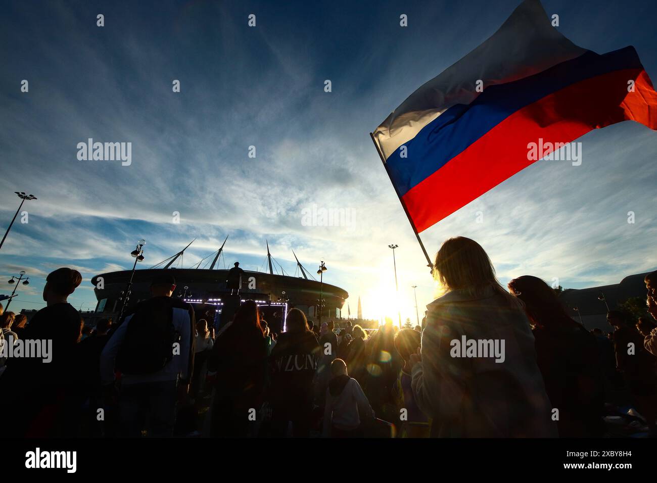 12. Juni 2024, St. Petersburg, Russland: Die Bürger feiern den Russland-Tag, indem sie während der Feierlichkeiten in St. Petersburg die russische Flagge schwenken, während das Stadion der Gazprom Arena im Hintergrund steht. Viele zeremonielle Veranstaltungen fanden in St. Petersburg am Russland-Tag statt. Am Nachmittag fand im Alexandergarten der 'Ball der Nationalitäten' statt. Am Abend begann ein festliches Konzert auf dem Territorium der Peter-und-Paul-Festung unter Beteiligung des Gouverneurs von St. Petersburg, Alexander Beglov. Auf dem Gelände der Festung gab es verschiedene Themenspielplätze sowie Meisterclasse Stockfoto