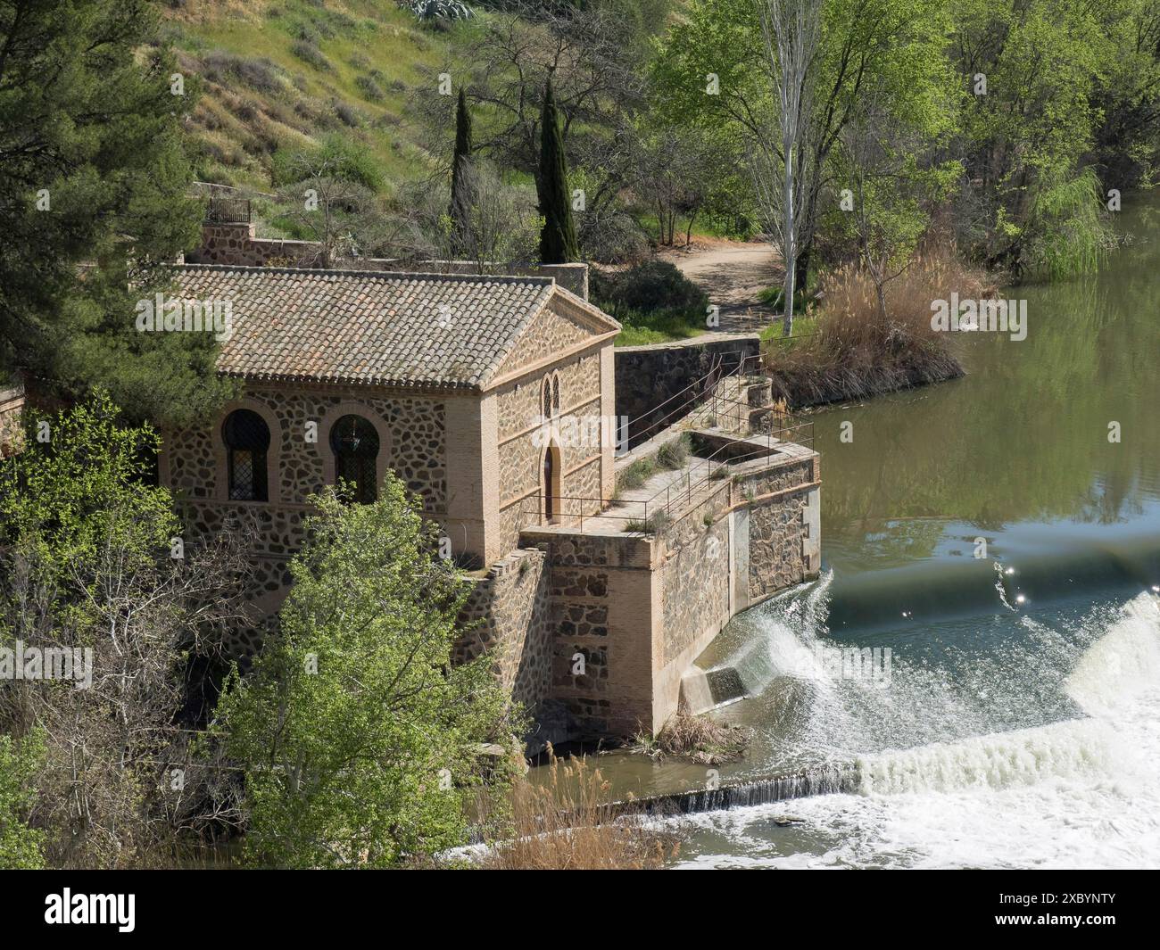 Kleines historisches Gebäude am Flussufer mit kaskadendem Wasserfall, umgeben von einer Frühlingslandschaft, Toledo, Spanien Stockfoto