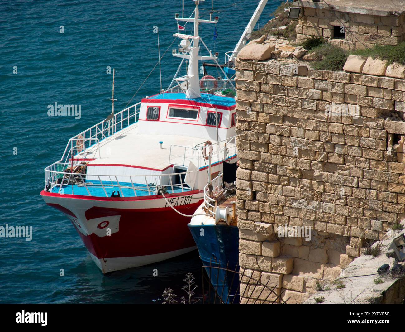 Rotes Schiff in blauem Wasser neben einer Steinmauer in einem Hafengebiet, valetta, mittelmeer, malta Stockfoto