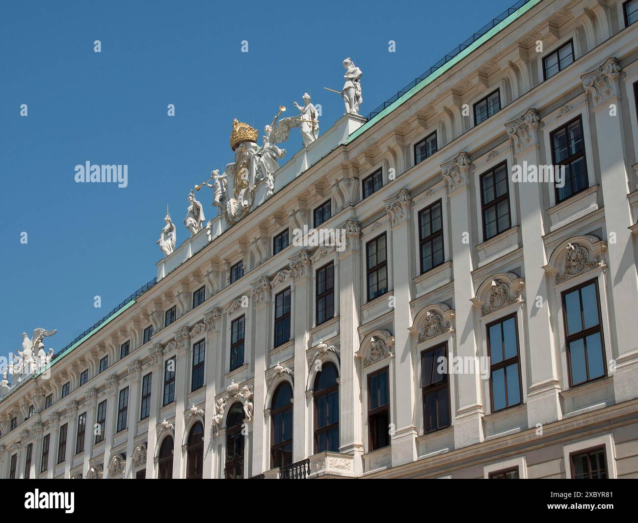 Weißes Barockgebäude mit Statuen auf dem Dach, vielen Fenstern und klarem blauem Himmel, Wien, Österreich Stockfoto