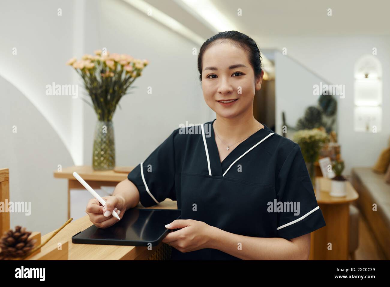 Porträt des lächelnden vietnamesischen Spa-Salons an der Rezeption, der ein Dokument auf einem digitalen Tablet unterzeichnet Stockfoto
