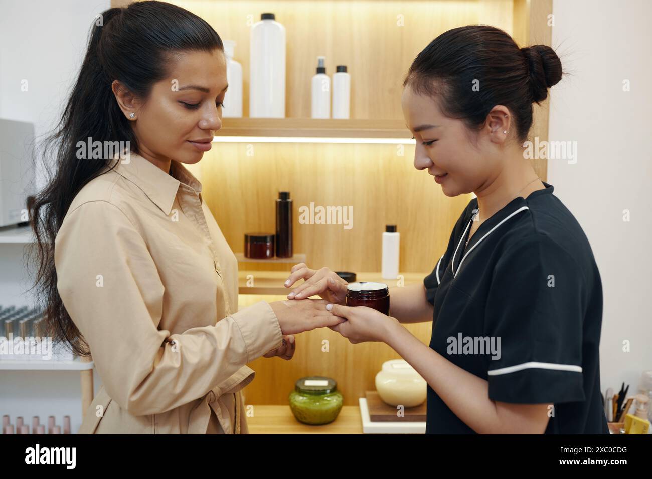 Kosmetikerin, die duftende Körpercreme auf der Hand des Kunden aufträgt Stockfoto