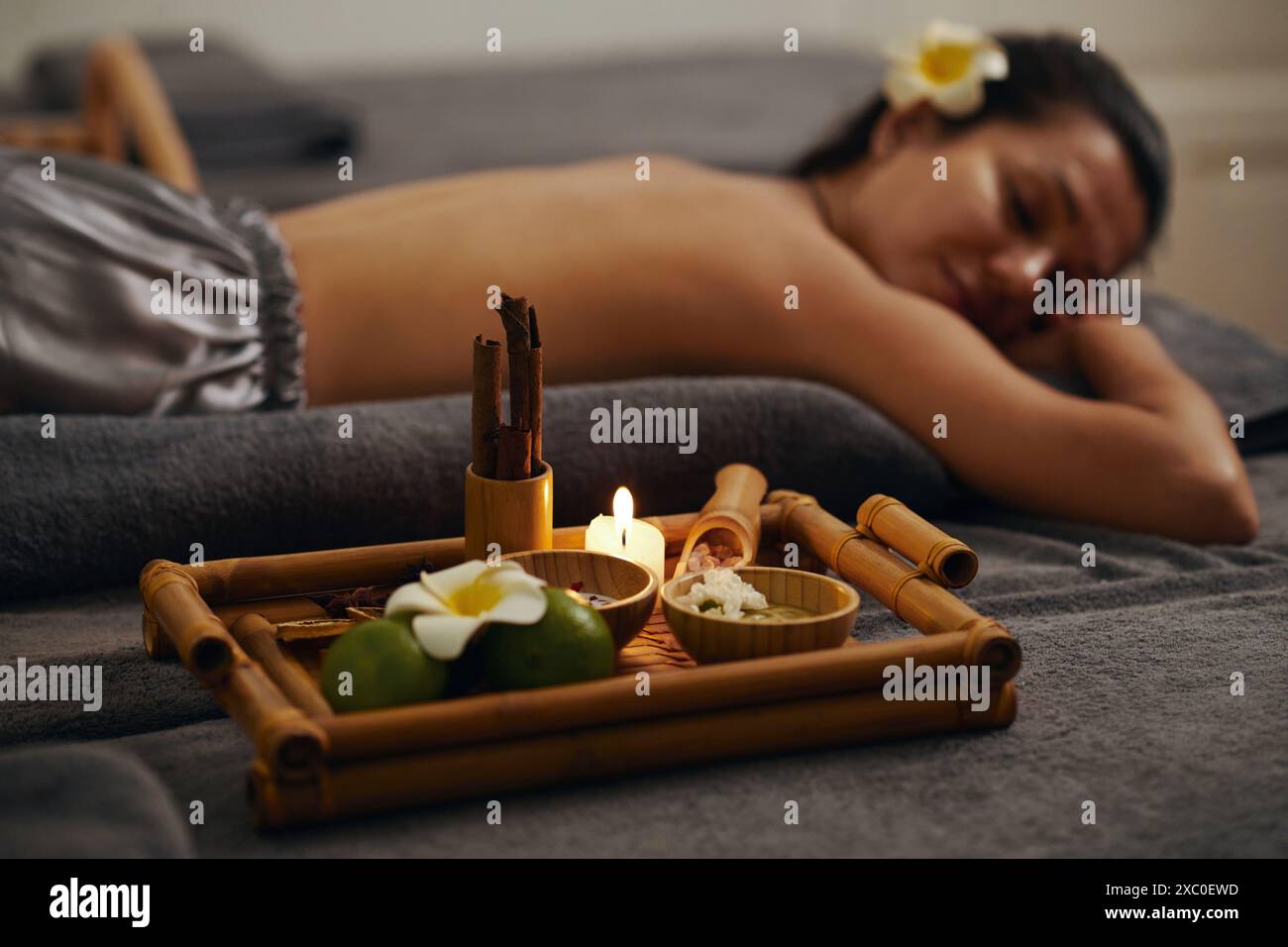 Tablett mit brennenden Kerzen und duftendem Salz auf Bambustablett neben der jungen Frau, die eine Spa-Massage bekommt Stockfoto