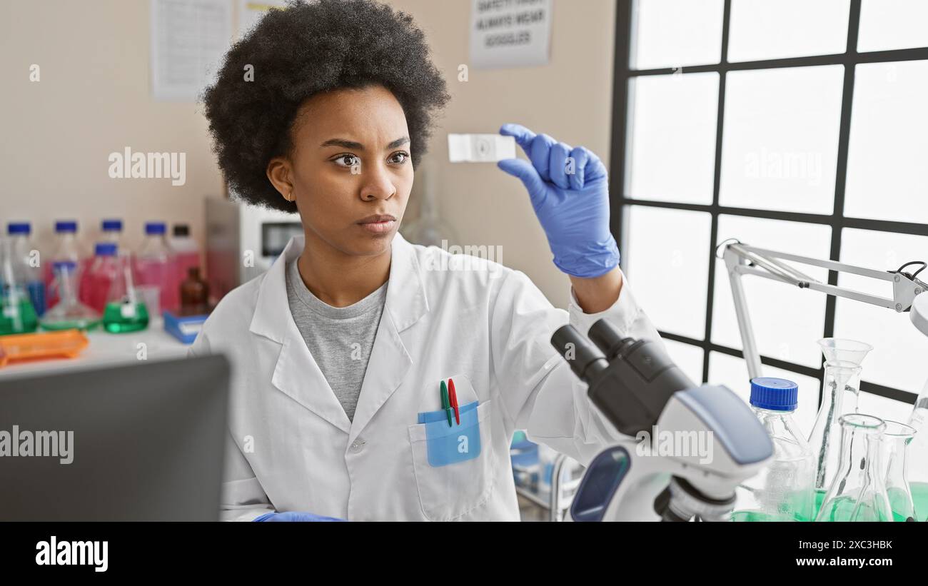 Eine fokussierte afroamerikanische Wissenschaftlerin analysiert einen Objektträger im Labor und demonstriert dabei Fachwissen und Präzision. Stockfoto