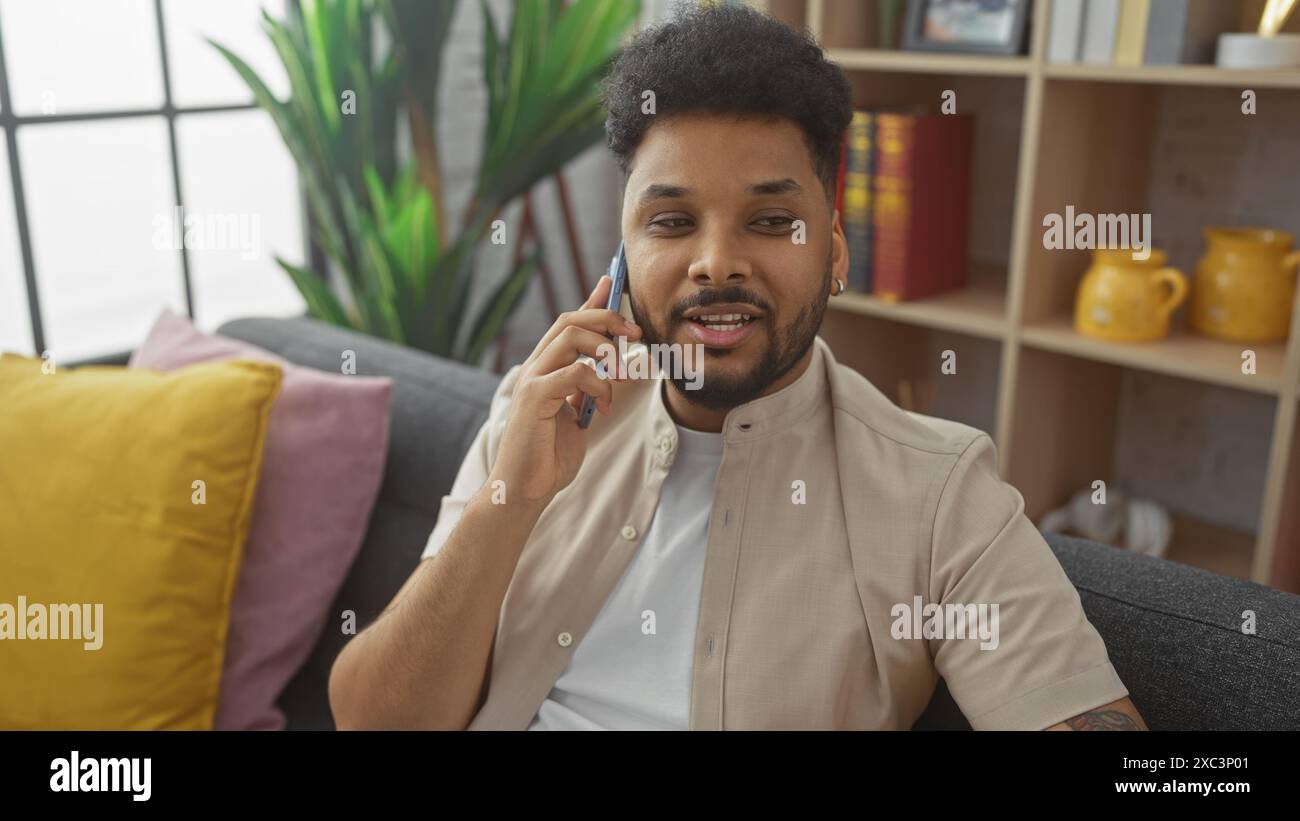 Afrikanischer Mann lächelt während eines Telefonats in einem gemütlichen Wohnzimmer mit moderner Einrichtung Stockfoto