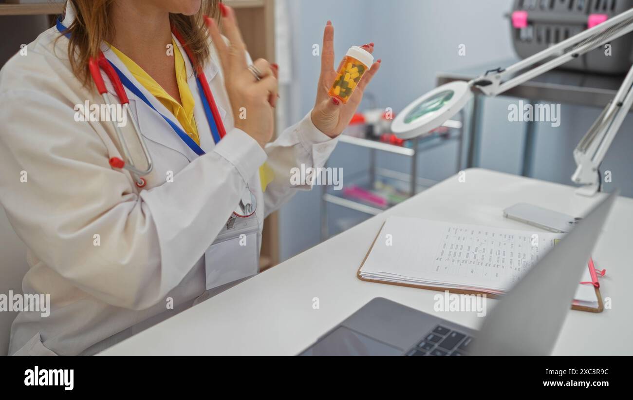 Eine Ärztin in einer Klinik erklärt Medikamente mit einer Pillen-Flasche, ihre Hände zeigen, während ein Notebook, ein Laptop und ein Stethoskop auf der Th sichtbar sind Stockfoto