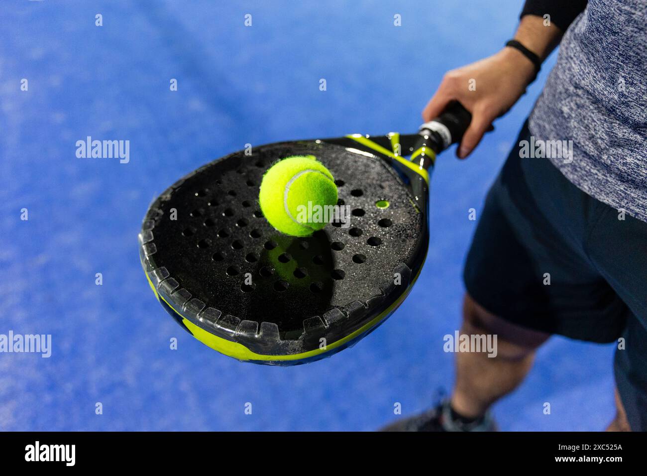 Ein Paar schwarze Schläger auf einem blauen Padel-Platz mit einem gelben Ball Stockfoto