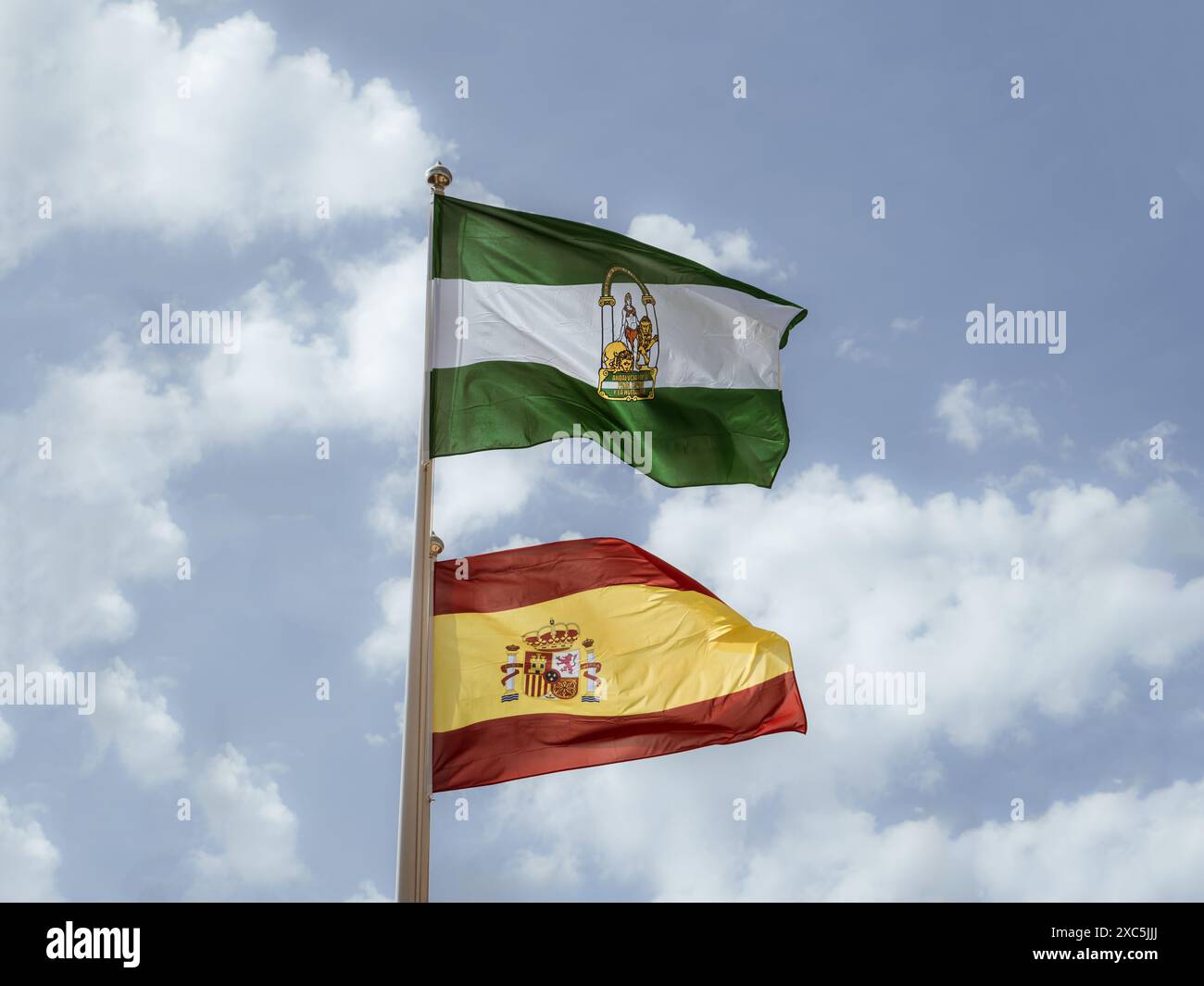 Foto der Flaggen Spaniens und Andalusiens (Espana und Andalusien) vor dem bewölkten blauen Himmel, nationale und regionale Flaggen Stockfoto