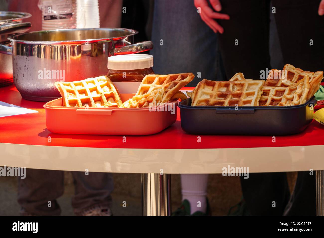 Ein Tisch für ein Picknick, mit Waffelbehältern, einem Stapel Pfannkuchen, einem Schokoriegel und anderen Picknickutensilien. Stockfoto