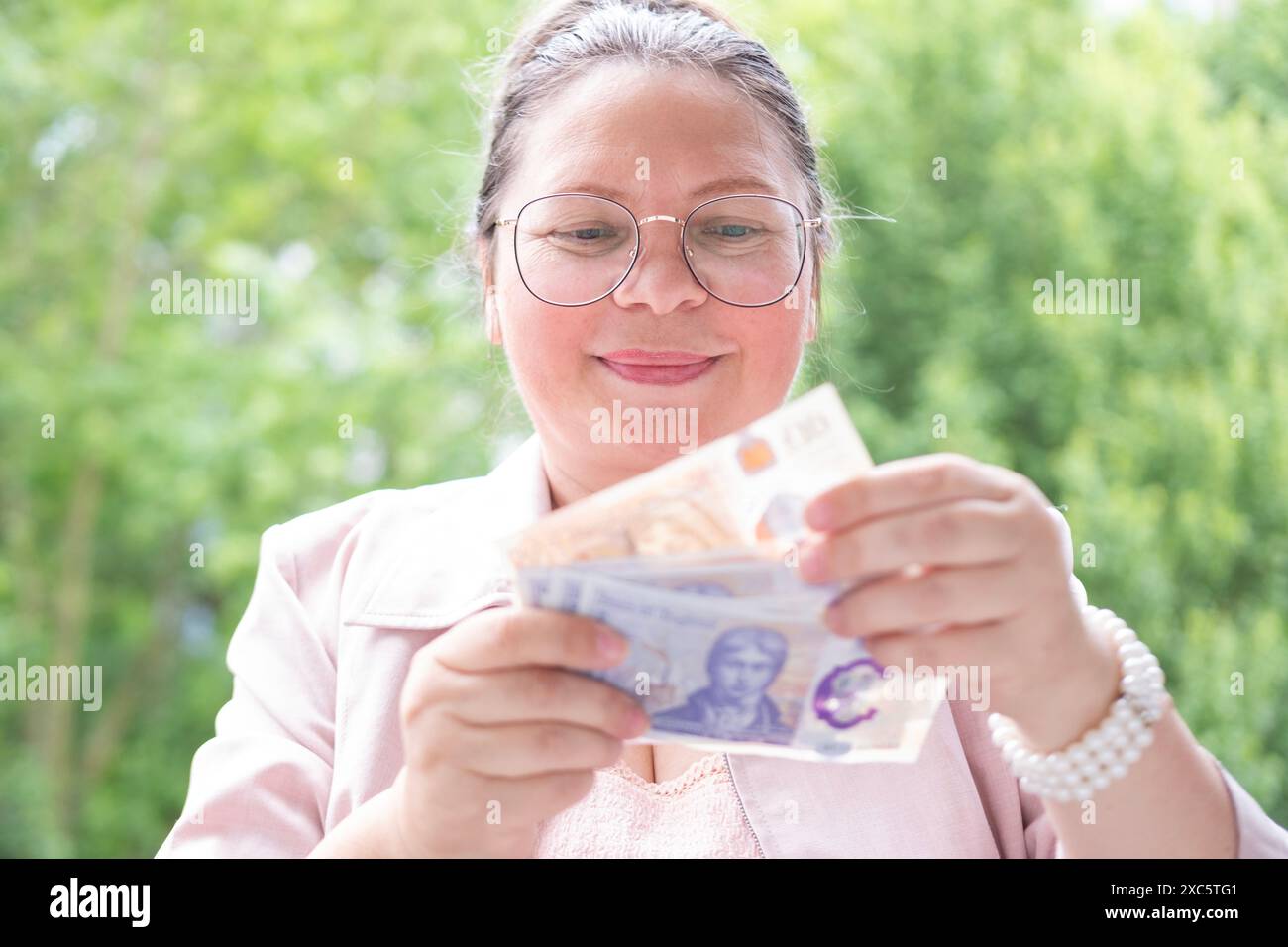 Zufriedene Frau, die Geld hält, englische Pfund-Rechnungen zählt, freut sich über Erfolg, antizipiert, was sie ausgeben soll, fördert gutes Finanzverhalten Stockfoto